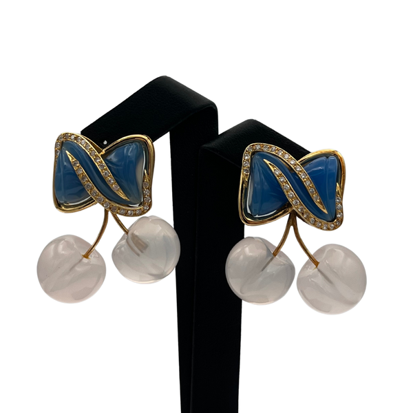 Pair of earrings with blue and pink cherries and white spherical elements on a black stand.