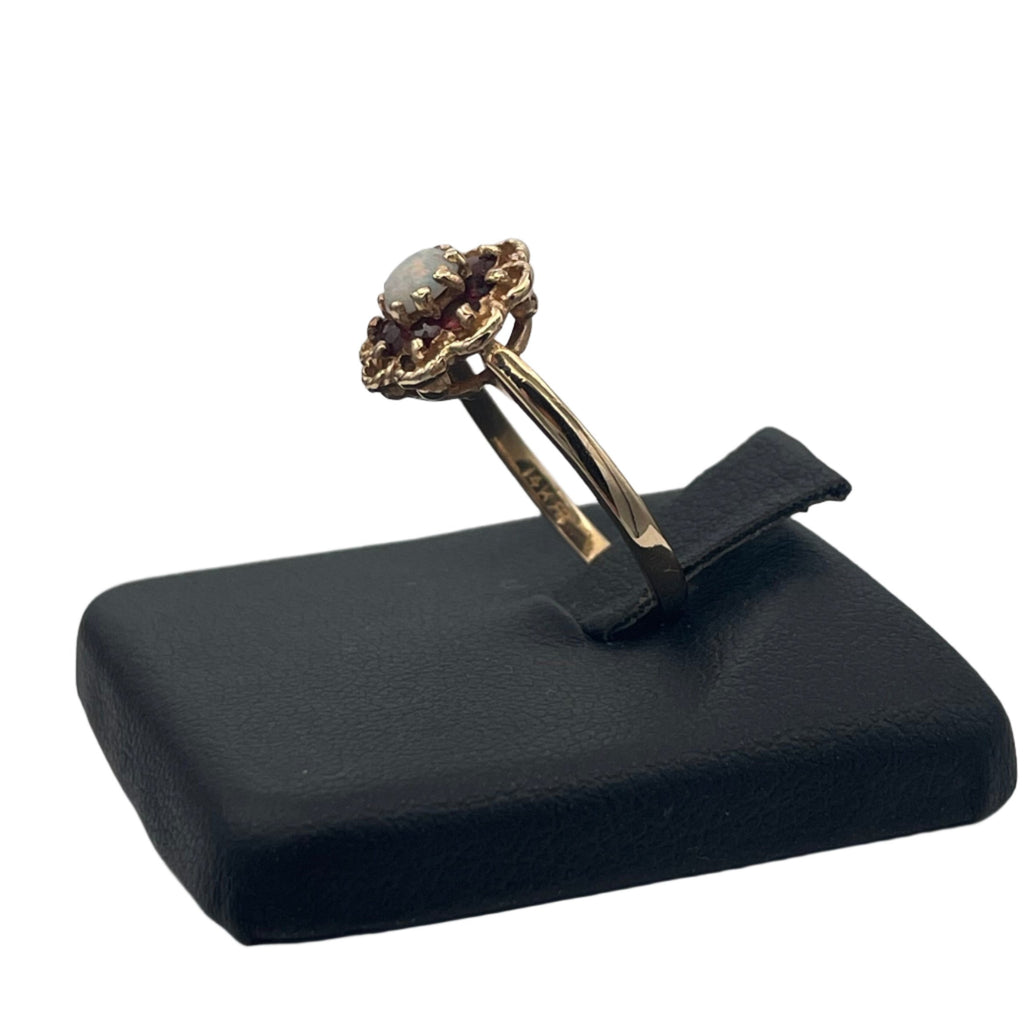 Lovely 14K yellow gold ring. A beautiful opal is set in the heart of the flower and 8 small garnets serve as petals in an openwork decor.